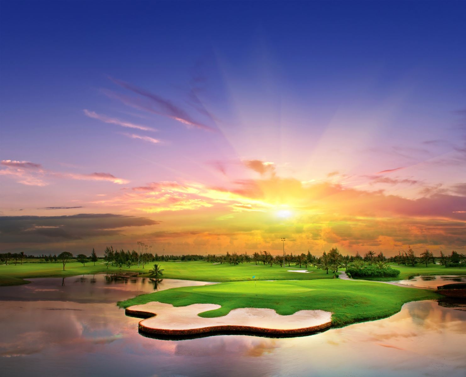 A golf course with a body of water and a sunsetDescription automatically generated