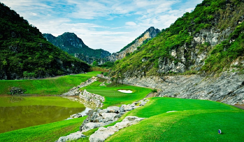 A golf course with water in the middle of a rocky mountainDescription automatically generated